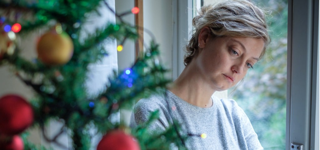 A woman feeling sad and waiting next to a Christmas tree