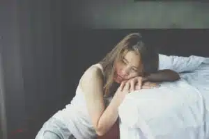 asian woman sitting alone on the floor in the bedroom leaning her head against the bed
