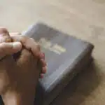 Christian life crisis prayer to god. Man Pray for god blessing to wishing have a better life. man hands praying to god with the bible. believe in goodness. Holding hands in prayer on a wooden table.