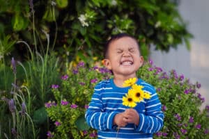 young boy smiling big while holding yellow flowers