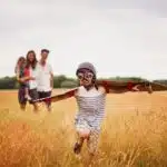 family standing in a field. little kid with cardboard wings, running