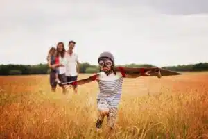 family standing in a field. little kid with cardboard wings, running