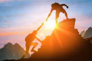 person helping another person up a mountain top